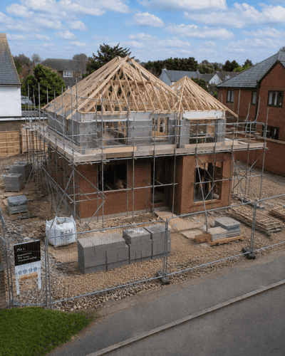 New build house structure rising with scaffolding and brickwork. Roof structure formed on two-storey detached new build property